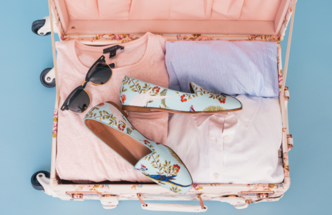Avoin matkalaukku, jossa aurinkolasit, kukkakengät ja vaatteita.
