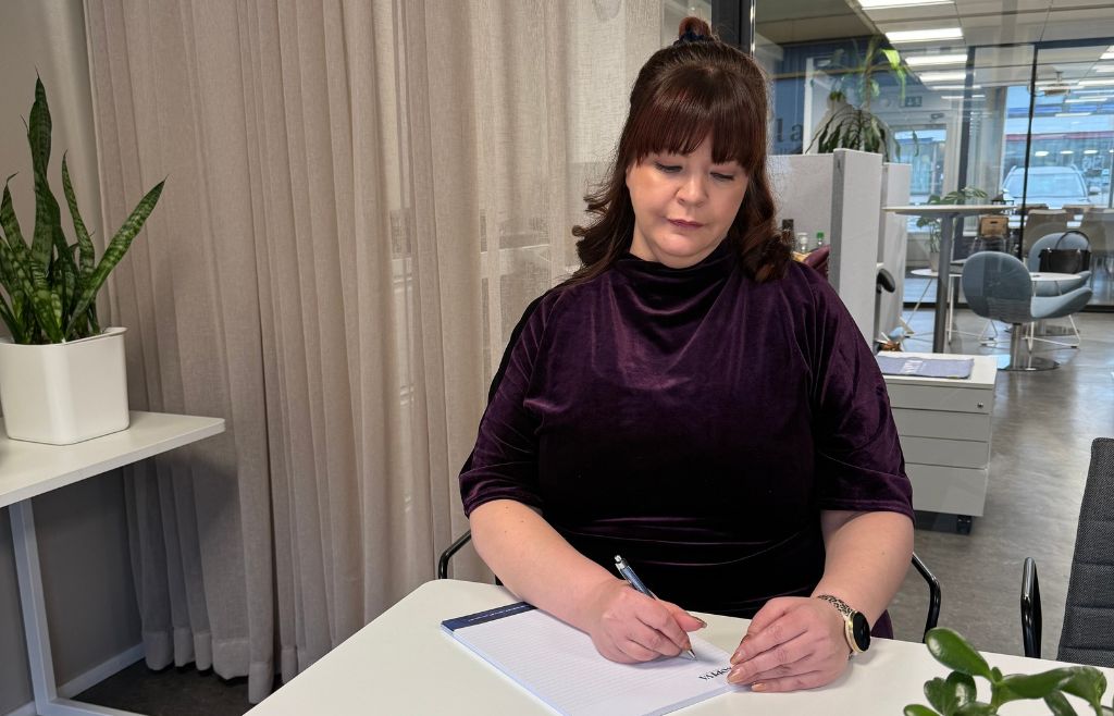 Marjaana kirjoittamassa muistiinpanoja lehtiöön pöydän ääressä.