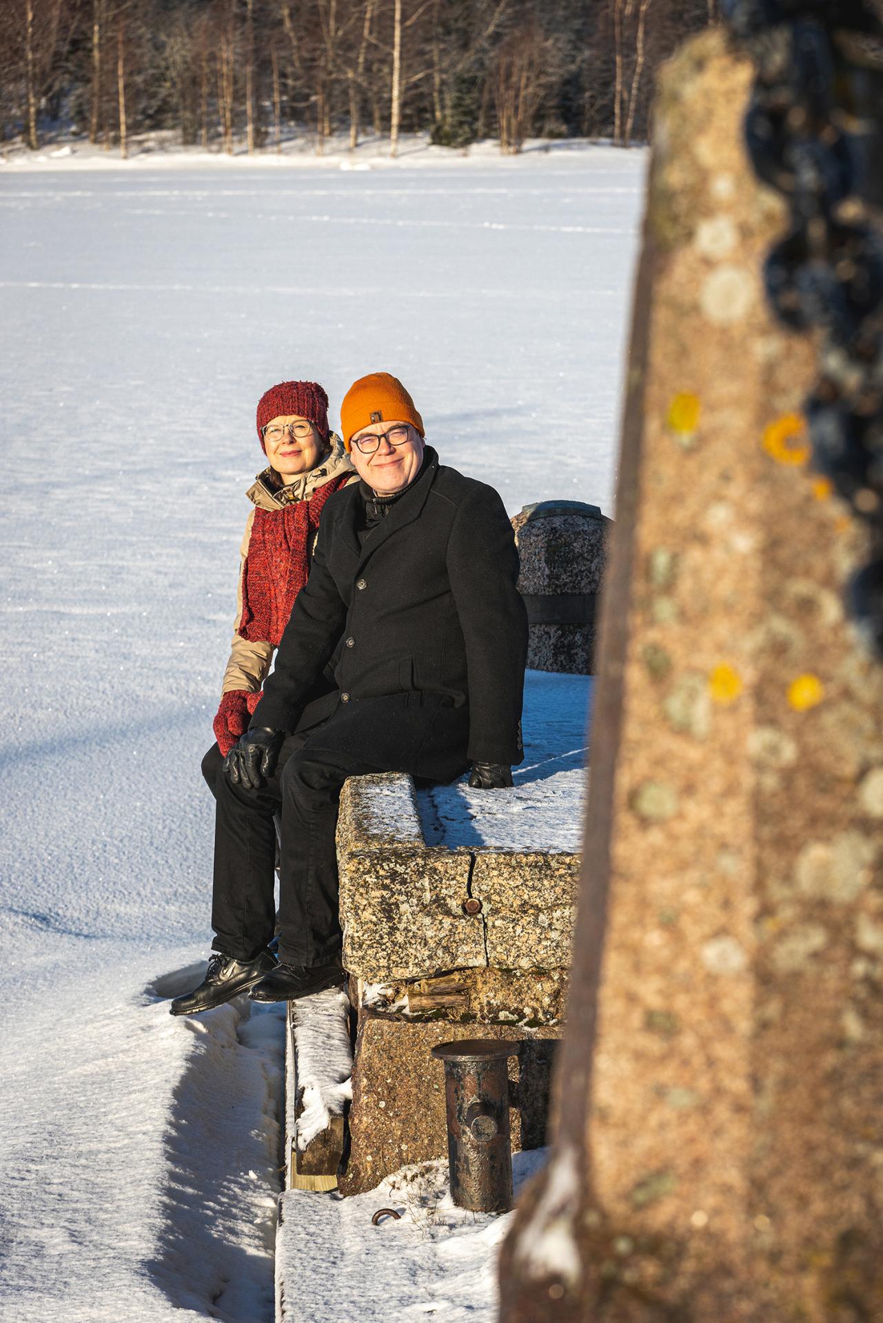 Kaksi henkilöä istumassa laiturilla talvella.