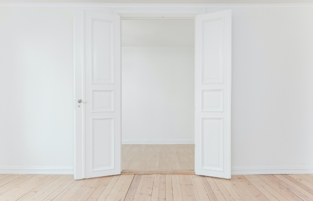 Tyhjä valkoinen huone, jossa avoin ovi.